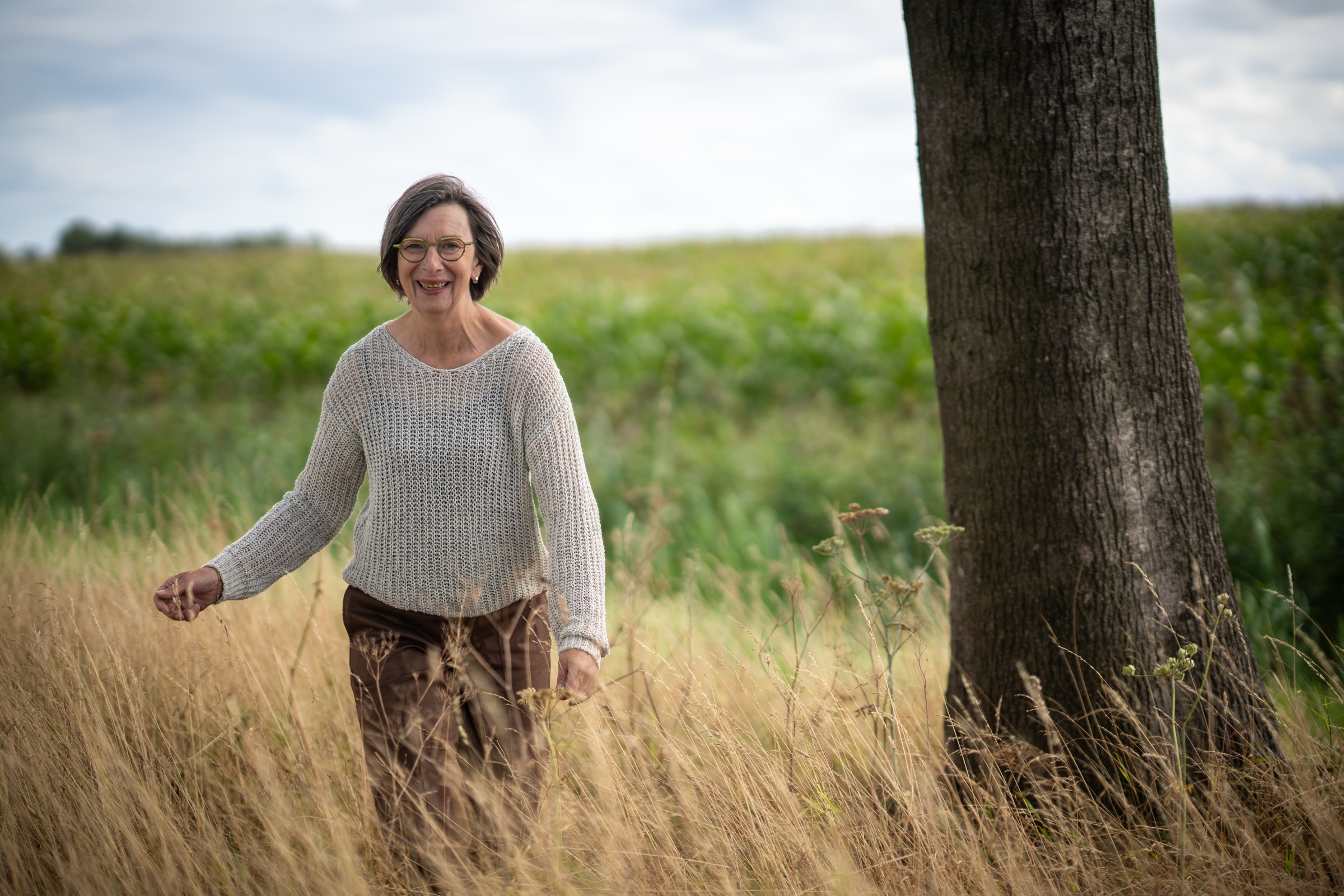 Rita van der Laag loopt lachend door het hoge gras bij een boom